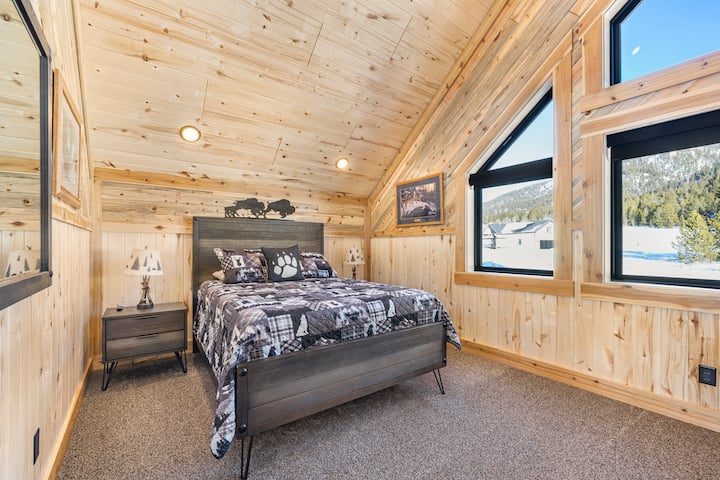 Cozy mountain-style bedroom featuring a comfortable bed, rustic wood finishes, large windows with scenic views, and a TV—perfect for a peaceful night’s rest after exploring.