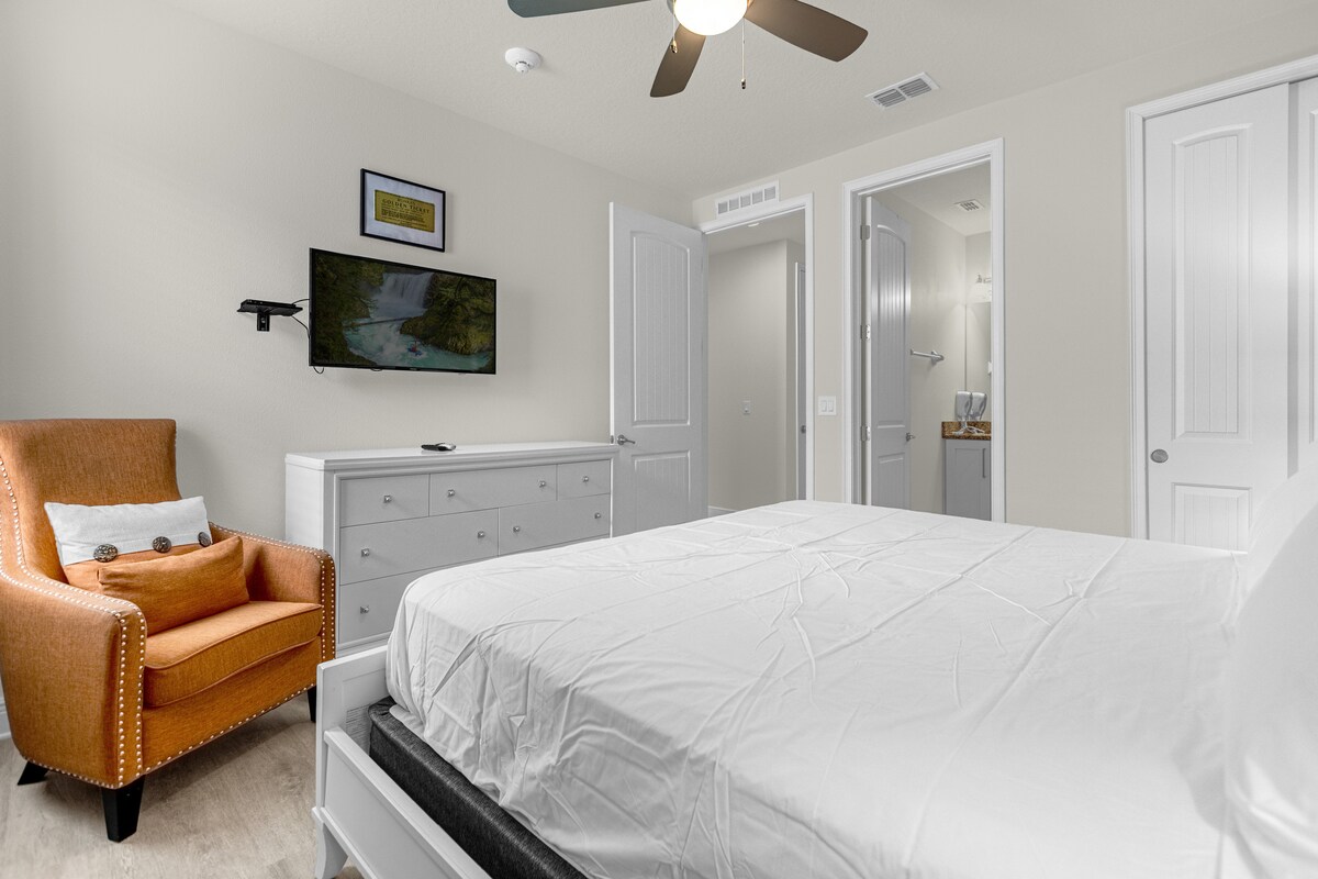 חדר שינה מקסים עם מיטה נוחה, כיסא לוסון נעים וטלוויזיה עם מסך שטוח המותקנת מעל מגירה מסוגננת. תאורת רוגע יוצרת אווירה מרגיעה, ויוצרת את מקום המפלט המושלם למנוחה והתחדשות במהלך השהייה.