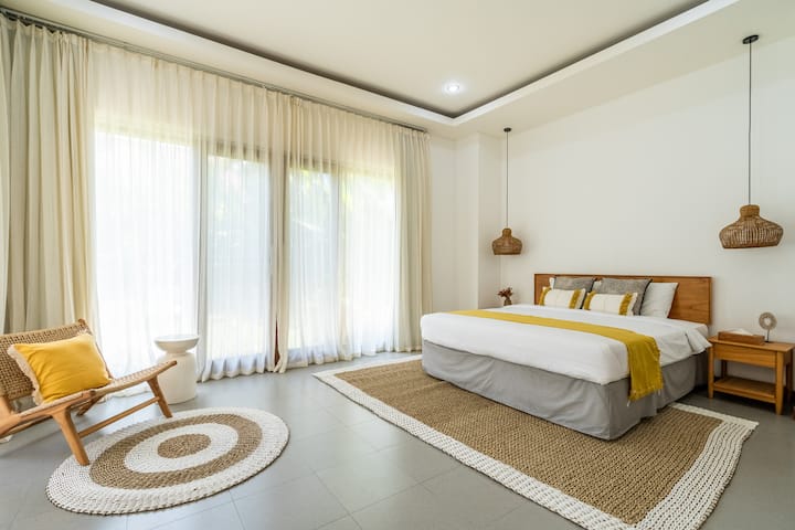 The ground-floor master bedroom at Villa Savanna offers a spacious retreat with a king bed, an ensuite bathroom complete with a bathtub, and tranquil views of the pool and lush garden.