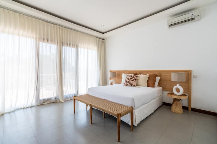 Bedroom #2 at Villa Savanna, located on the second floor, offers a spacious retreat with a king bed, ensuite bathroom, cozy couch, private balcony, and tranquil views of the pool and lush garden.