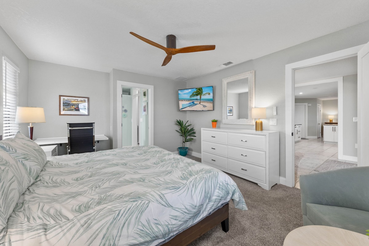 The primary bedroom features a king bed with a Zinus Green Tea Luxe mattress for exceptional comfort & support; a 50” 4K TV, seating area, fold-down workspace with leather chair, and an ultra-quiet ceiling fan with remote for a restful night’s sleep.