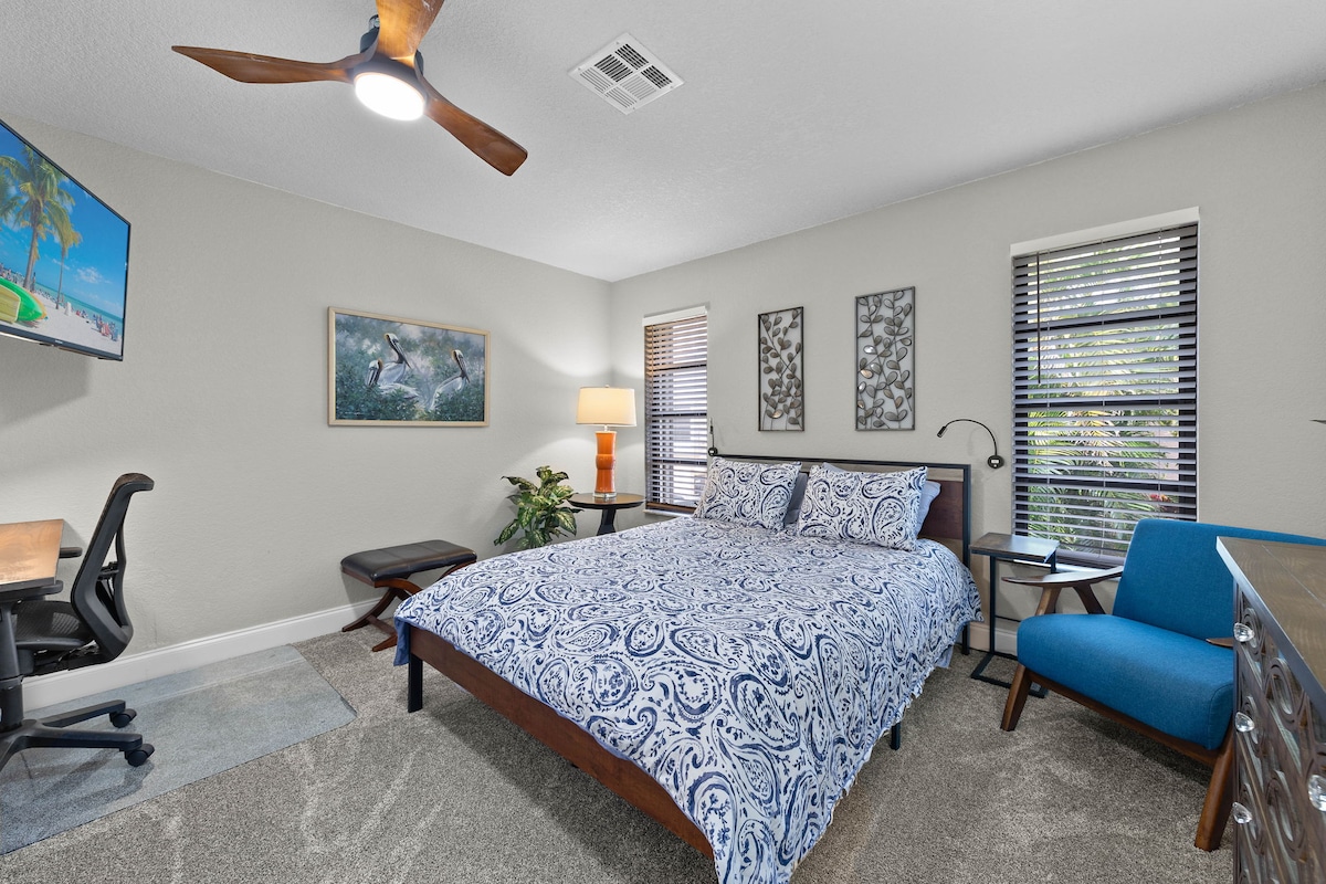 Bedroom 2 has a queen-sized bed and separate seating for reading and relaxing. The lighting is varied, with a desk lamp, a midcentury table lamp, and reading lights on each side of the bed, with built-in charging ports.