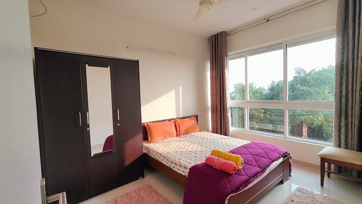 تتميز غرفة النوم هذه بسرير مريح متوسط الحجم، تكمله خزانة ملابس واسعة ونافذة كبيرة تجلب إطلالة مريحة على المساحات الخضراء المورقة، مما يخلق جوًا هادئًا وهادئًا.