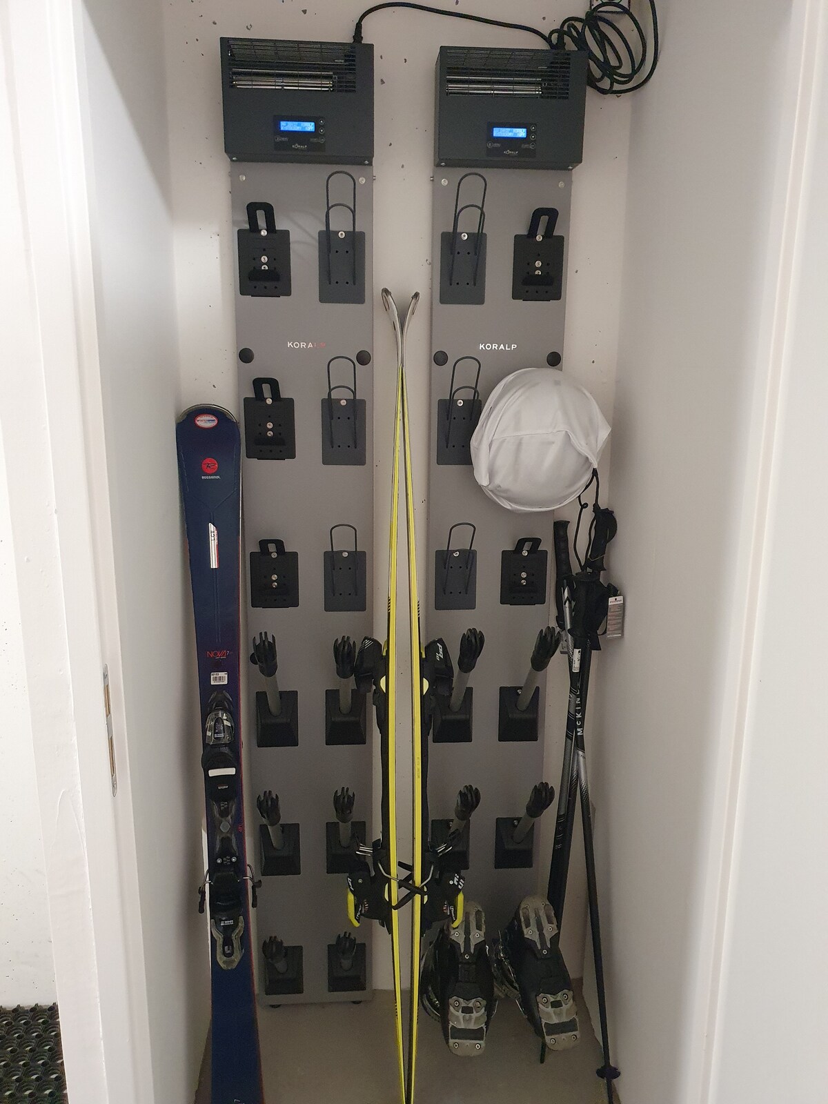 A ski storage area is visible, featuring multiple hooks for skis, poles, and accessories. Two heat units are mounted at the top, providing warmth for gear. The space is organized and designed for convenient access to winter sports equipment.