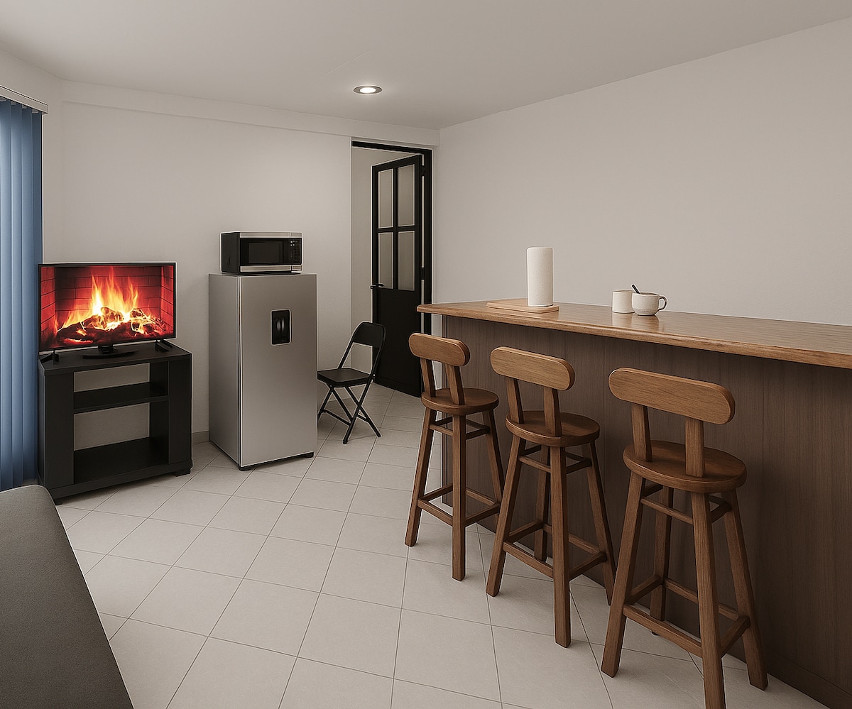 A compact living area includes a bar with three wooden stools, a television displaying a fireplace, and a microwave next to a refrigerator. A folding chair is set against the wall, and a door leads to another space, all illuminated by soft overhead lighting.