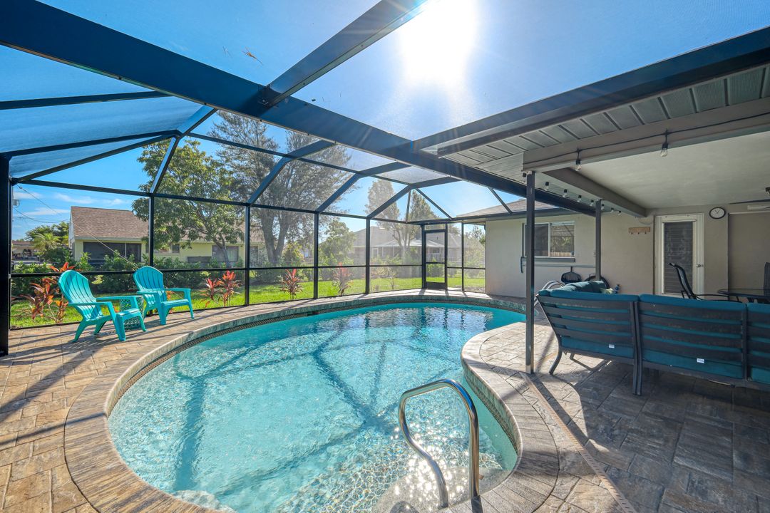 A heated pool is surrounded by a screened lanai, featuring comfortable outdoor seating and vibrant landscaping. Sunlight reflects off the water, illuminating the area. Two lounge chairs are positioned near the pool, creating an inviting space for relaxation.