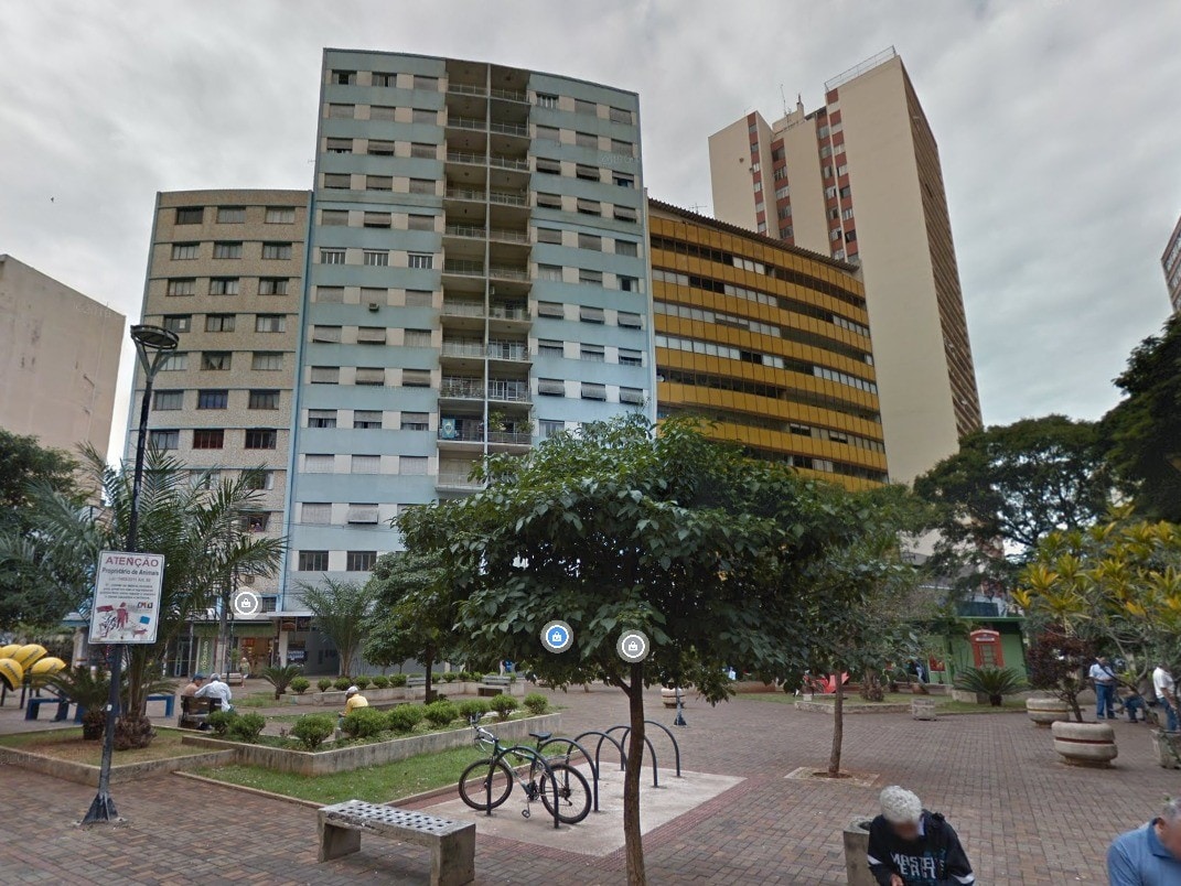 A courtyard setting features multiple high-rise buildings surrounding a green area. Trees and benches are arranged alongside a bike rack, contributing to a communal atmosphere. The space is paved with brick, providing clear pathways for pedestrians.
