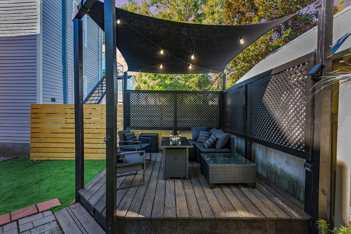 A private backyard deck features cozy seating arrangements with stylish outdoor furniture. Soft lighting from twinkle lights adds a warm glow. The space is enclosed by decorative lattice screens, creating an inviting atmosphere for relaxation and gatherings.