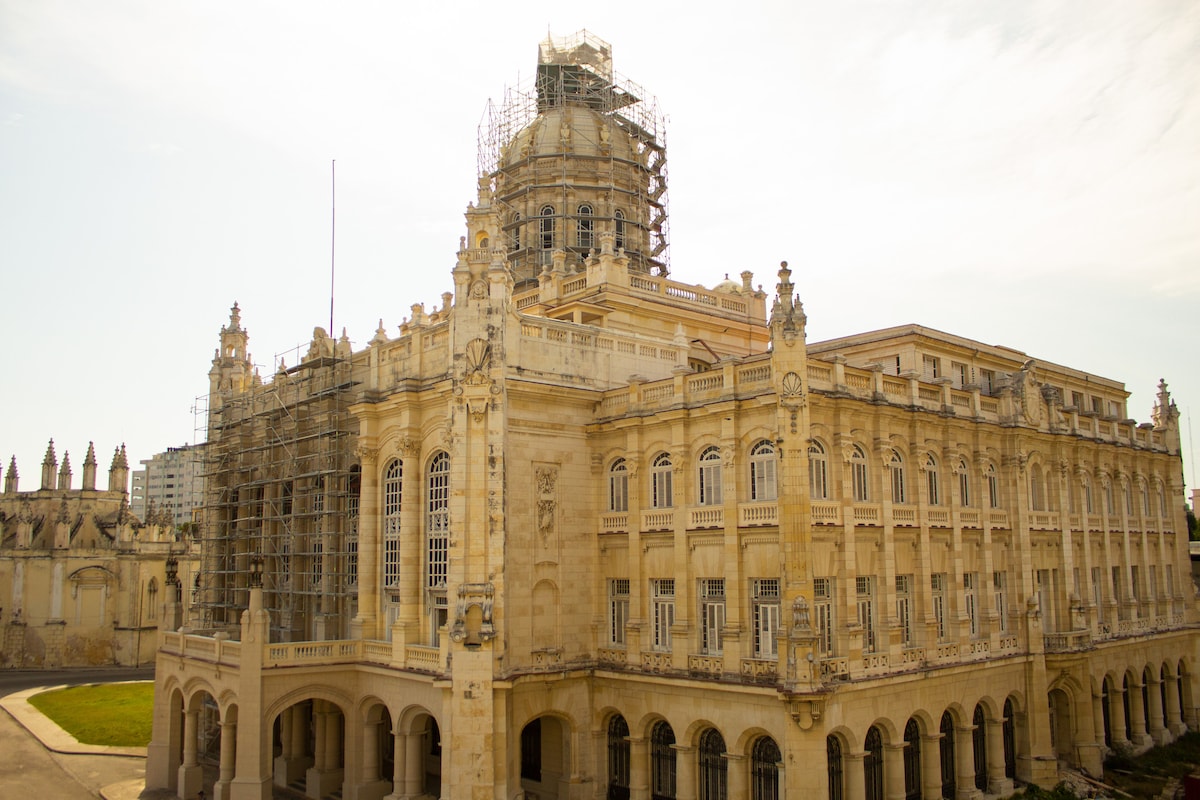 The Museum of the Revolution is showcased with its grand, neoclassical architecture, featuring intricately designed façades and a large dome. Scaffolding surrounds parts of the building, indicating ongoing restoration work. The structure is set against a clear sky, highlighting its historical significance and architectural details.