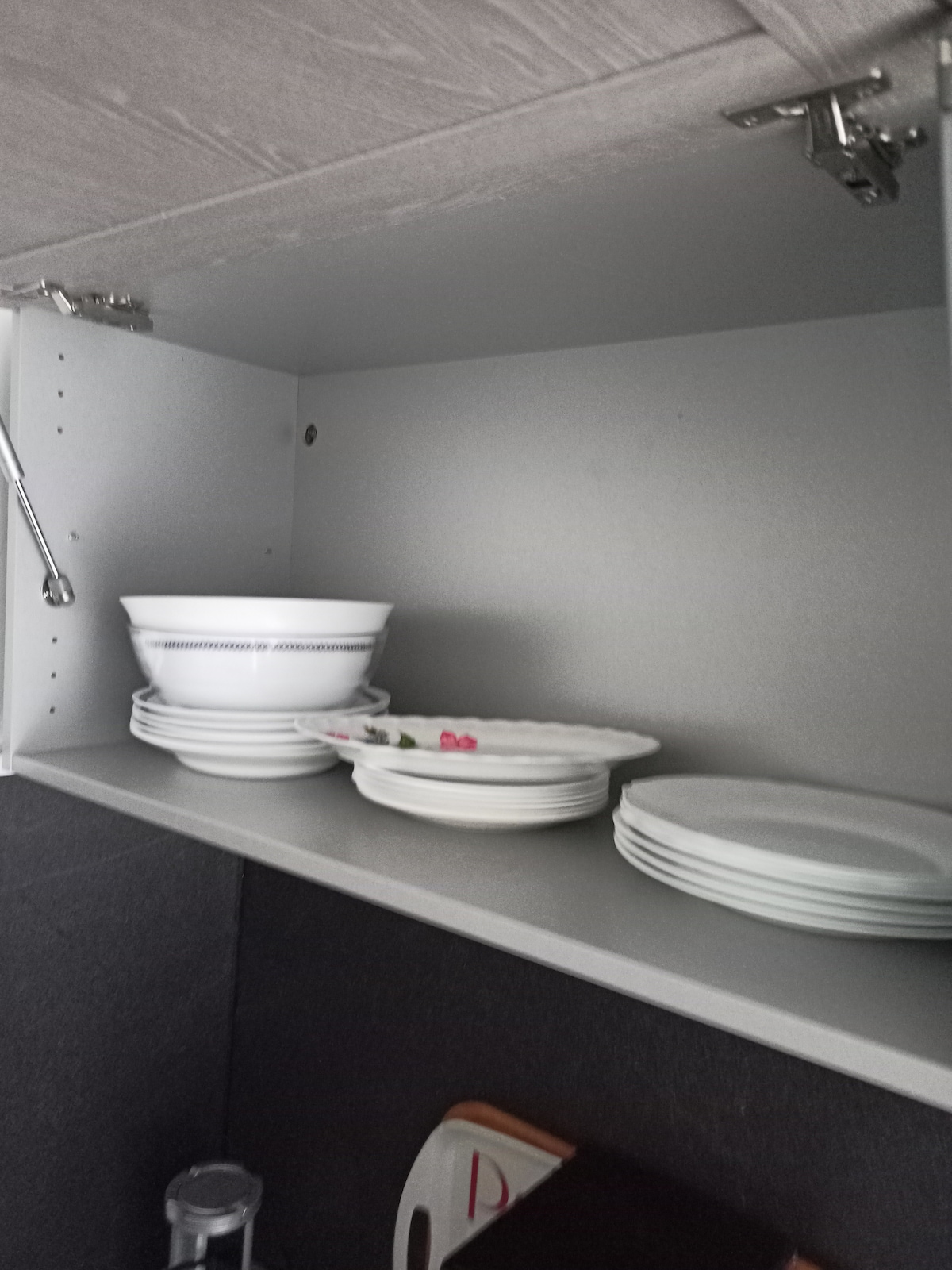 A neatly organized kitchen cabinet is visible, featuring several white plates stacked on a shelf. Above, a set of bowls is arranged, showing an additional decorative detail with a floral design on one bowl.