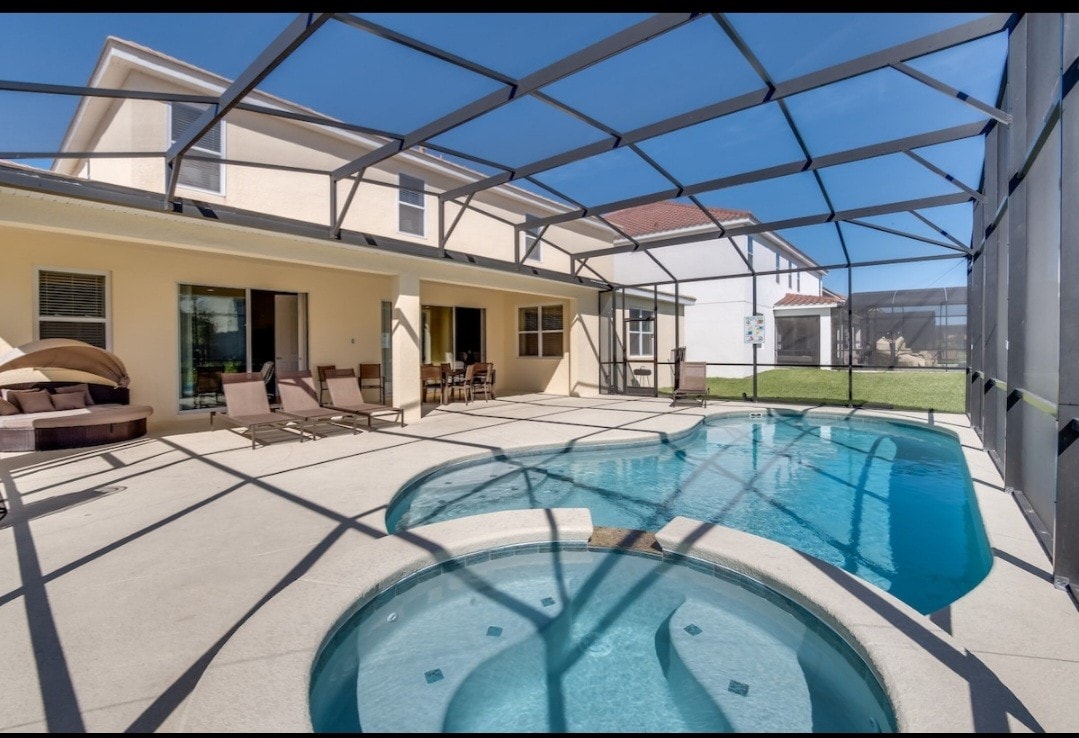 An outdoor area is highlighted by a screen-enclosed pool and spa. Sun loungers are positioned nearby, while a dining table accommodates several chairs. Natural light enhances the inviting ambiance of the space, surrounded by neatly trimmed grass and a view of neighboring homes.