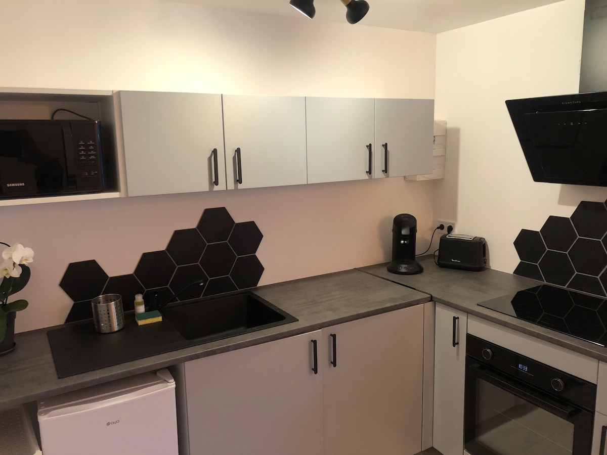 A modern kitchen is presented with sleek cabinetry in light and dark colors. The counter features dark hexagonal tiles and essential appliances, including a microwave, coffee maker, and toaster. A sink and a refrigerator are visible, contributing to a functional cooking space.