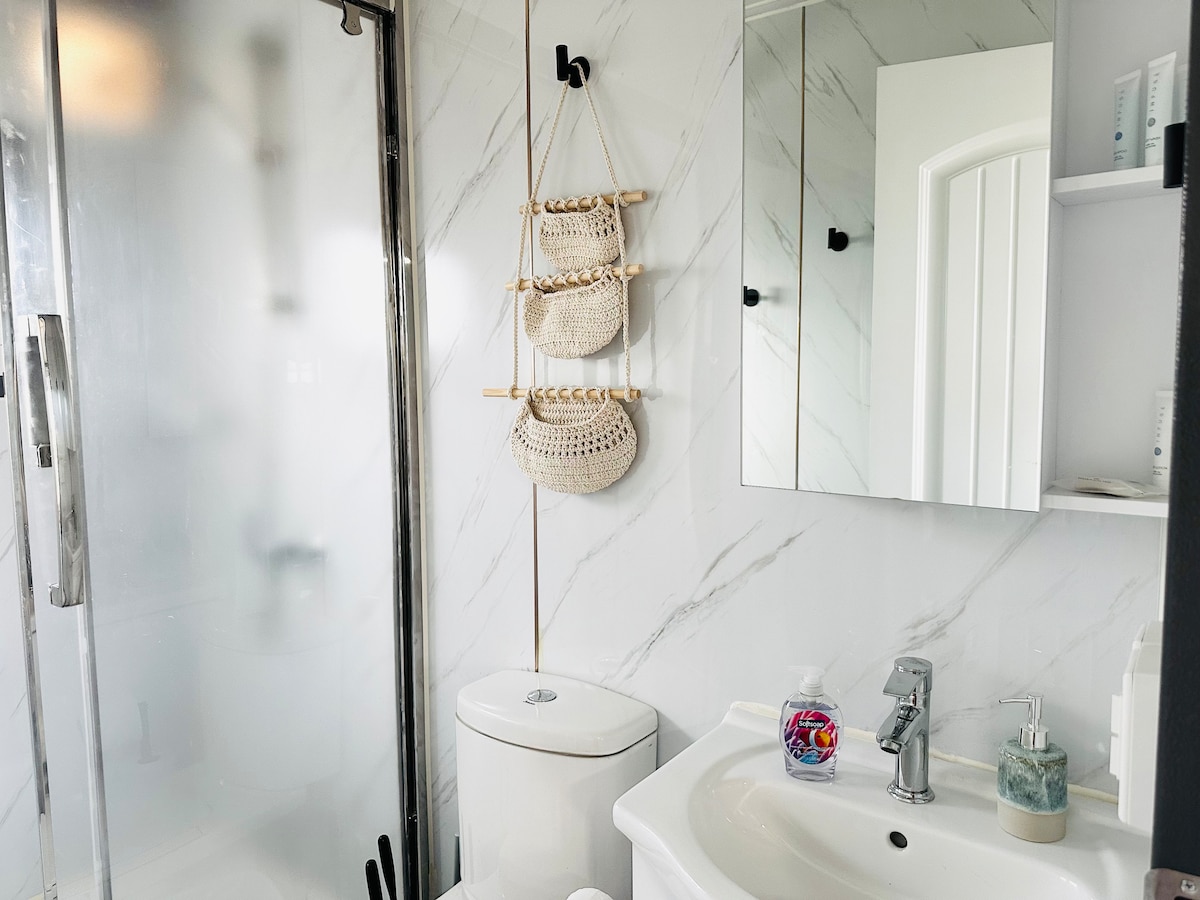 A stylish bathroom features a glass shower enclosed with clear panels. Decorative woven baskets are hung on the wall, adding texture. A modern sink with a polished faucet sits above a countertop, while mirror cabinets reflect the airy space. Personal toiletries are neatly arranged.