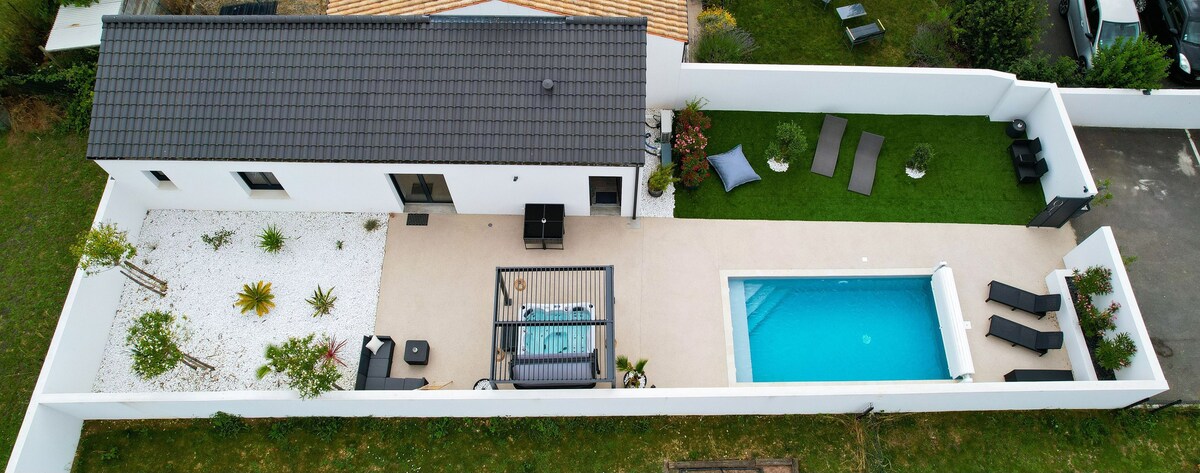 An aerial view of the property reveals a landscaped garden featuring a swimming pool and a jacuzzi. Surrounding seating areas are visible, including sun loungers positioned beside the pool. The well-maintained grounds are complemented by white stones and greenery, providing a serene outdoor space.
