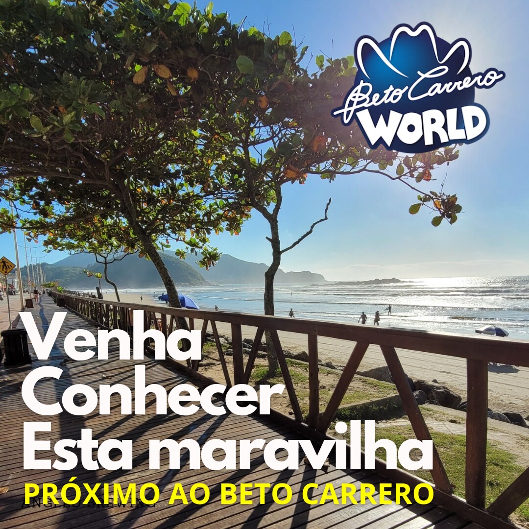 A wooden boardwalk stretches along the beach, offering a view of the calm ocean waves and distant mountains. Sunlight reflects off the water, enhancing the coastal scenery. The image includes signage promoting nearby attractions, inviting guests to explore the area.