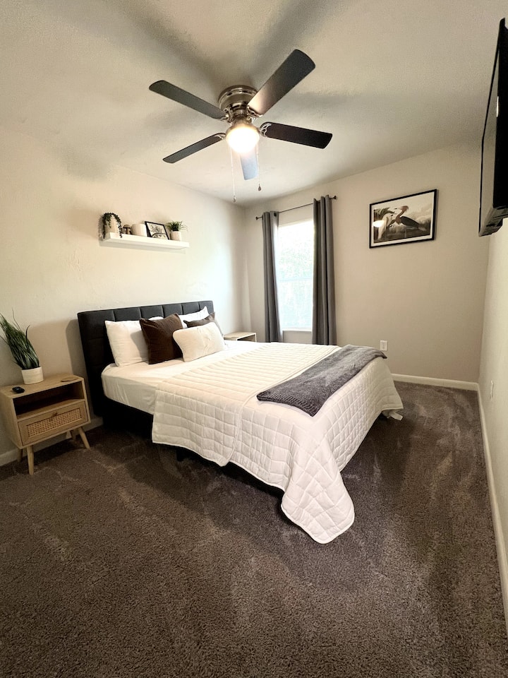 Elegante dormitorio limpio con cama tamaño queen y televisor inteligente Roku de 40 pulgadas.