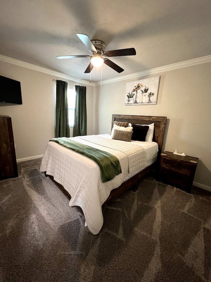 Elegante dormitorio limpio con cama tamaño queen y televisor inteligente Roku de 40 pulgadas.