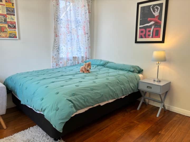 Საძინებელი 2, რომელზეც ნაჩვენებია საწოლი, საწოლისპირა მაგიდა და ლამპა, ხის იატაკი, ხელოვნება კედლებზე