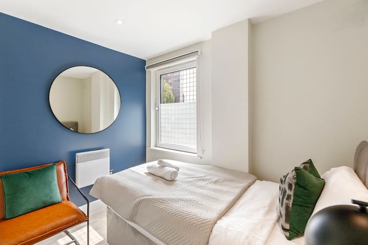 Očarujúca spálňa s jednou posteľou, okrúhlym zrkadlom na stene a malým oknom, ktoré prináša prirodzené svetlo, vytvára útulnú a príjemnú atmosféru pre pokojný pobyt.