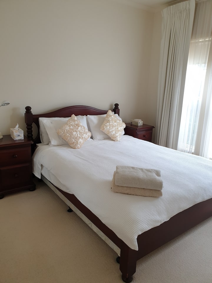 This bedroom comes with a queen-sized bed, a dark wooden bedside tables and headboard, floor to ceiling built-in robes with two mirrored robe doors, and an ornate triple window with block out curtains overlooking the beautiful front garden. 