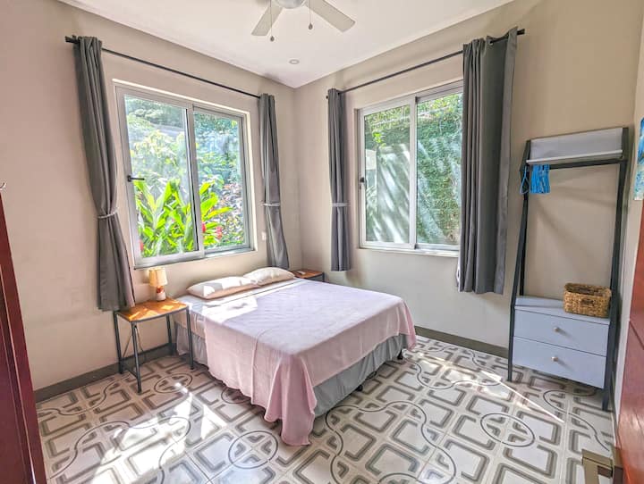 Krevat dopio "queen", 2 tavolina fundore dhe një dollap i pavarur me sirtarë dhe rafte. Bimët e dendura tropikale duken në dhomë nga të dyja dritaret.