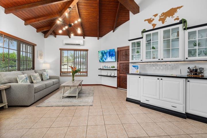Step into this airy and inviting living space, featuring vaulted wooden ceilings, a cozy sofa, and a Smart TV for group entertainment. Natural light floods through the large windows, creating a warm and tropical ambiance. Even a bar area!