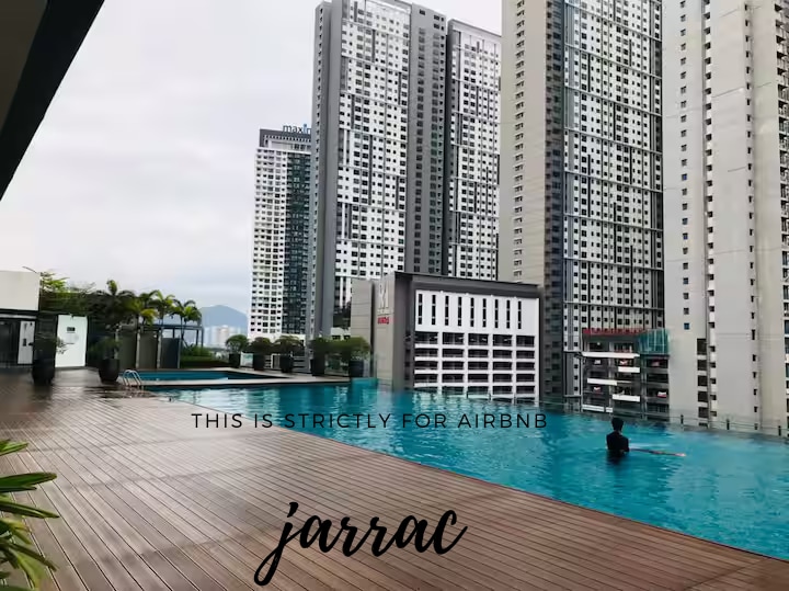 A spacious outdoor area features a sleek swimming pool surrounded by wooden decking. Towering buildings create a striking urban backdrop, with a person seen quietly enjoying the water. Lush greenery enhances the tranquil atmosphere, contributing to a refreshing environment for relaxation.