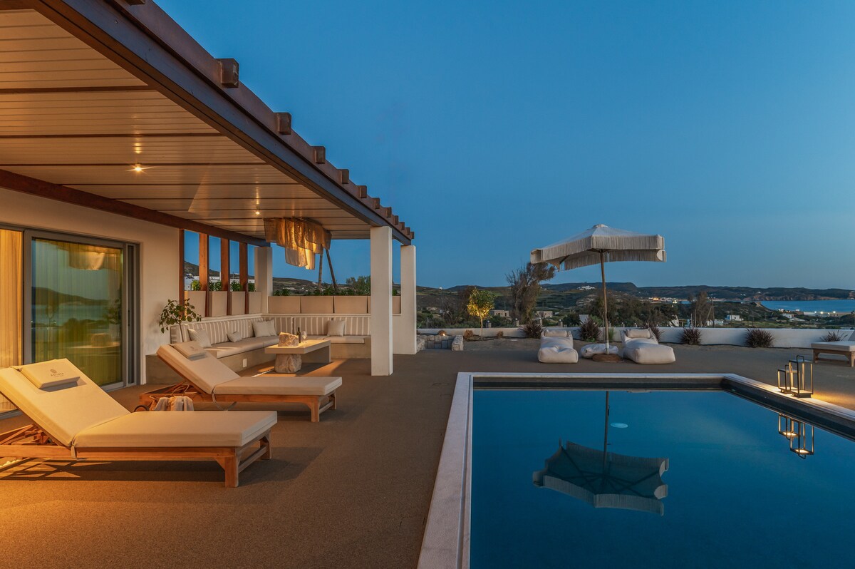 The outdoor patio features a private pool reflecting the twilight sky, with sun loungers positioned nearby. A shaded seating area offers a cozy spot for relaxation, complemented by soft cushions. The landscape provides an unobstructed view of the surrounding scenery, creating a serene environment.
