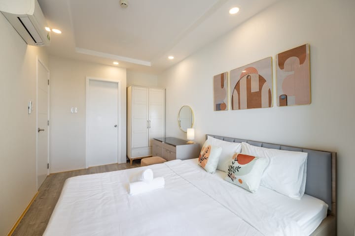 Un dormitorio principal con armario totalmente amueblado, escritorio de maquillaje, cama tamaño king, mesita de noche y lámpara de noche.