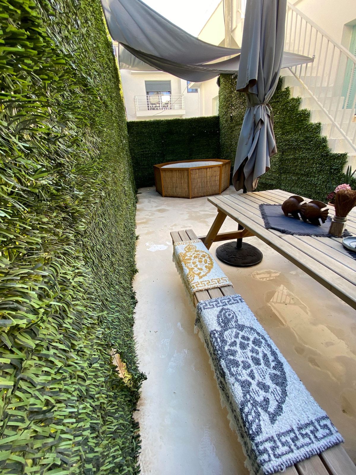 A private balcony is enclosed by lush greenery, providing a serene atmosphere. An outdoor hot tub is centered on a wooden deck, accompanied by a comfortable seating area. Soft natural light filters in, enhancing the tranquility of this peaceful retreat.