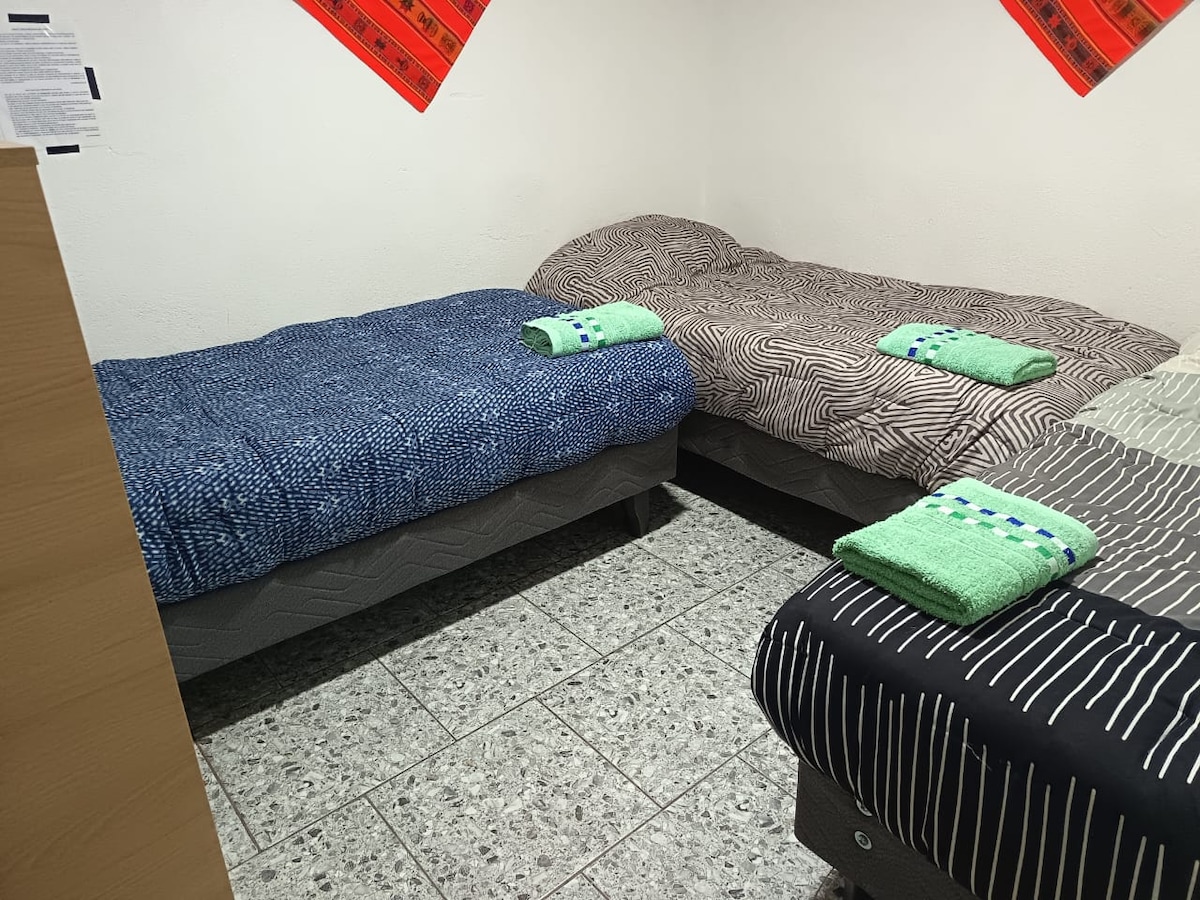 A cozy sleeping area is equipped with three beds, each adorned with patterned bedding. Two towels are neatly arranged on every bed, adding a touch of comfort. The floor features grey tiles, and a decorative element is visible on the wall above.
