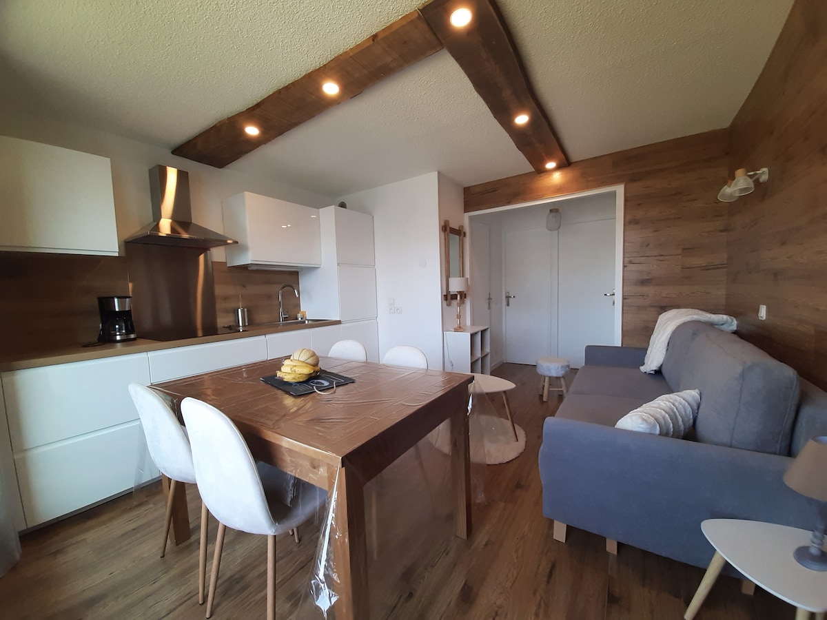 The main living area features a modern kitchen equipped with sleek cabinetry and stainless-steel appliances. A cozy seating area includes a quality convertible sofa. A dining table with four chairs is positioned next to the kitchen, creating a functional and inviting space for meals.