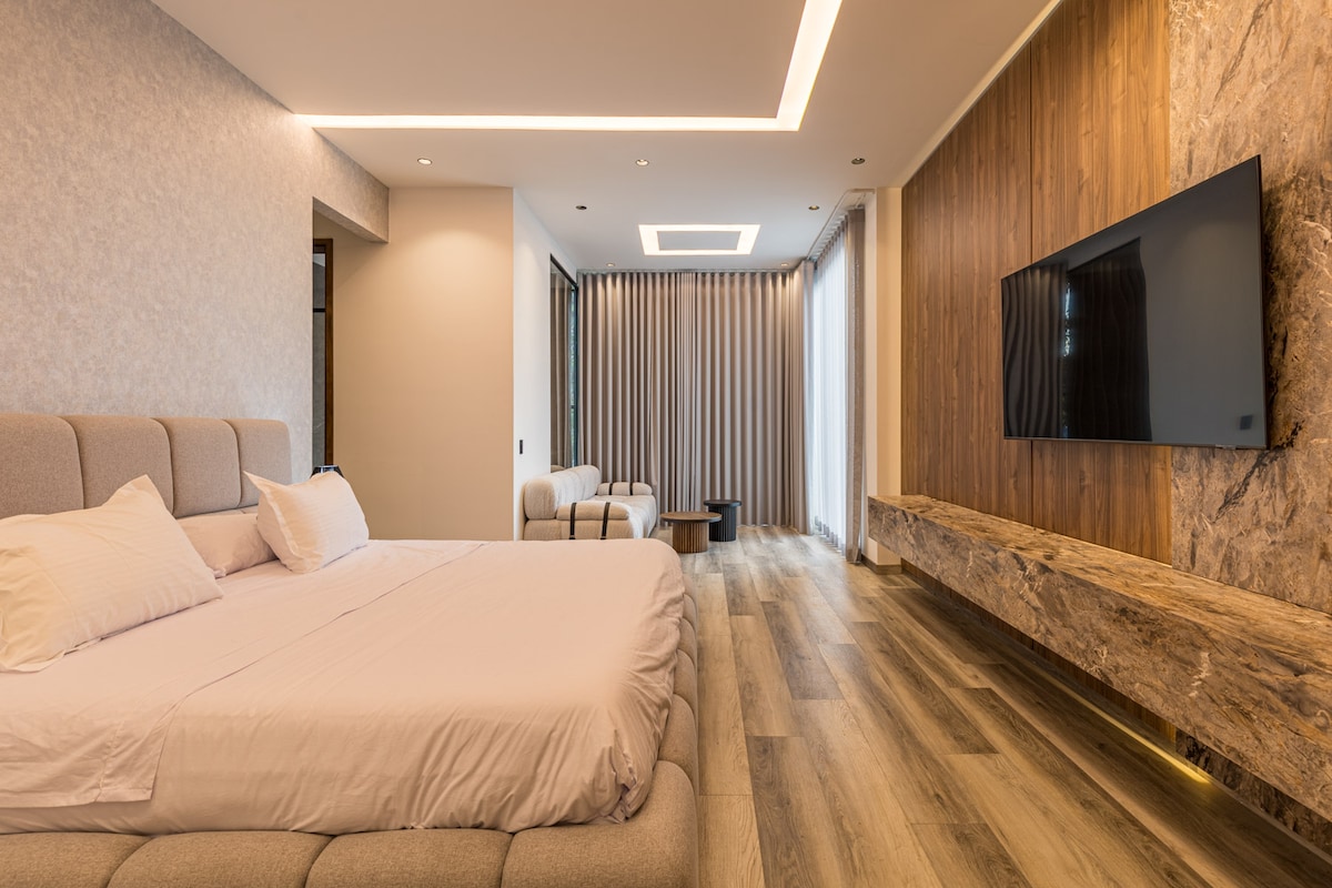 Retírate a este espacioso dormitorio con una cama tamaño king, iluminación ambiental suave, Smart TV y cortinas opacas, perfecto para noches de descanso y mañanas de pereza.