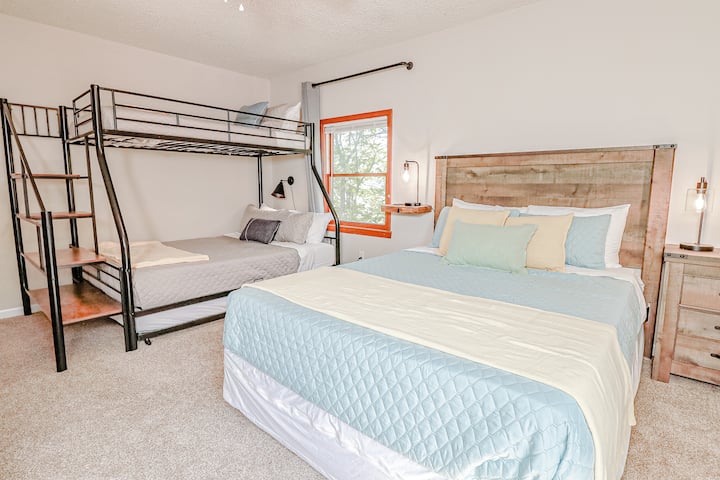 Queen bed + twin over full bunk bed. Twin floor mattress available on request (room sleeps max 5). There's a dresser, clothing rack, ceiling fan, and TV. Windows have light filtering mini blinds and room darkening curtains. Bathroom is next door.