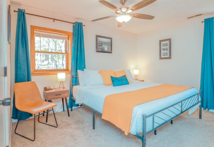 A king bed with dresser, closet, end tables, tv, ceiling fan, and a continental attached bathroom. The windows have light filtering mini blinds and room darkening curtains.