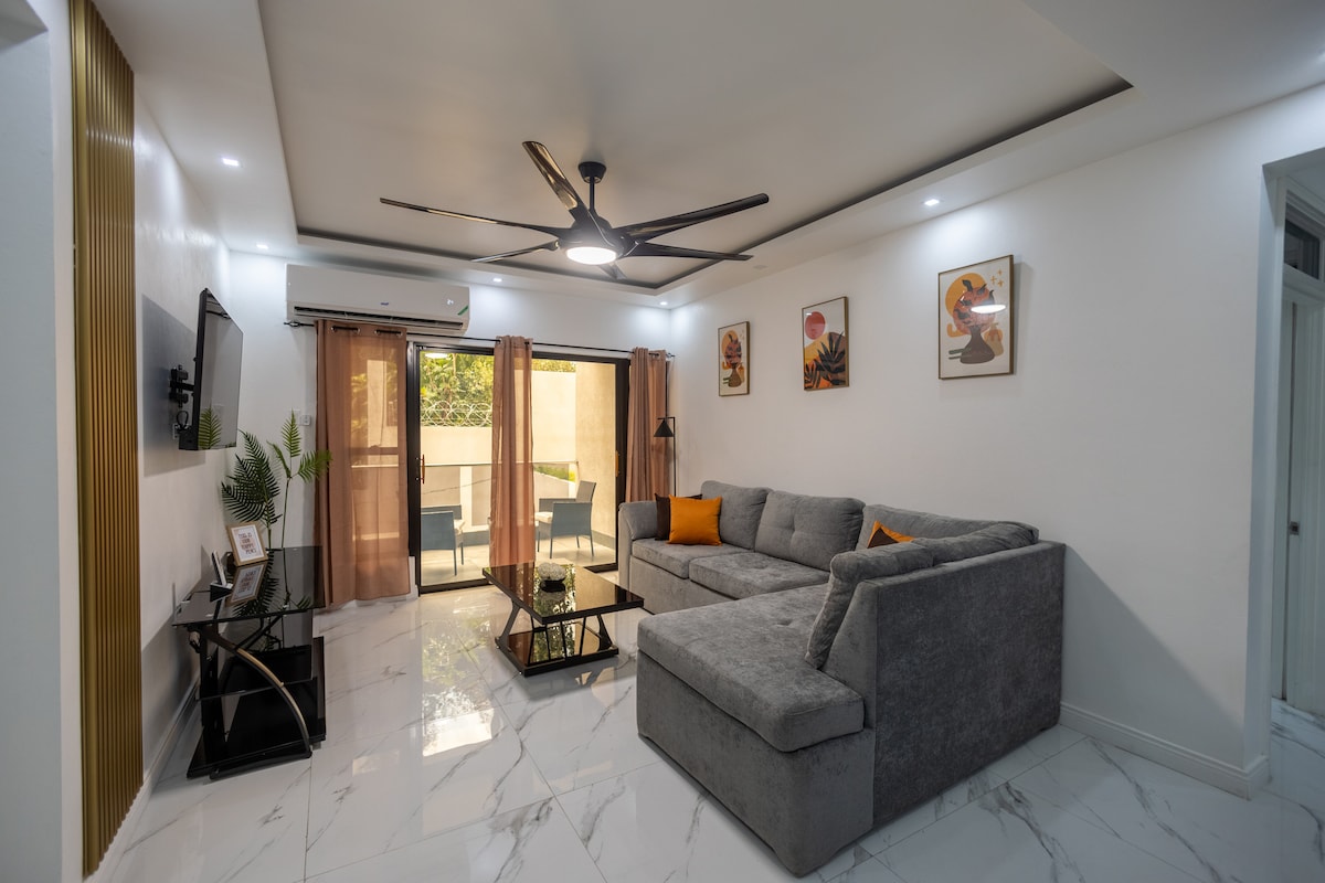 Დაისვენეთ ამ ფართო მისაღებ ოთახში ნაცრისფერი სექციური დივნით, შუშის ყავის მაგიდით და თანამედროვე დეკორით, რომელიც იდეალურია დასასვენებლად ან გასართობად.