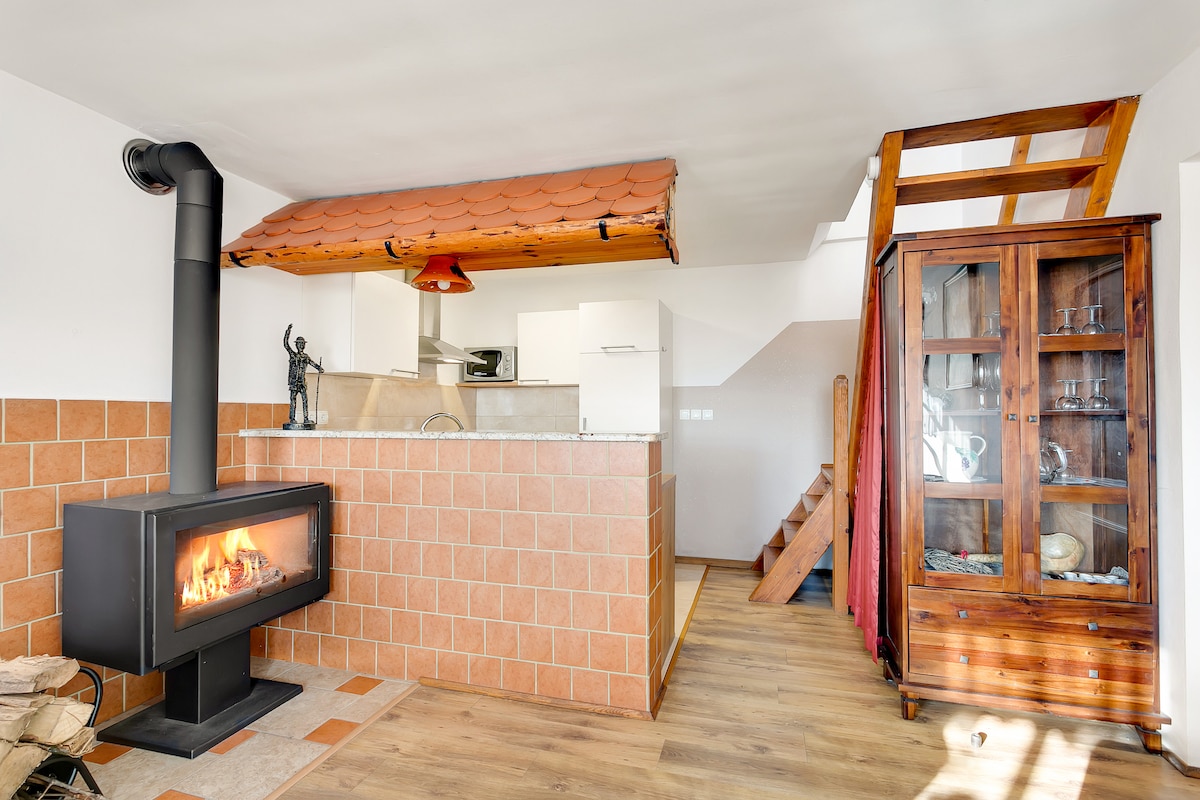 An inviting interior showcases a modern wood-burning stove as a focal point, with a tiled backsplash accentuating the warmth of the space. A wooden staircase leads to the upper level, while a glass-front cabinet displays decorative items, creating a cozy atmosphere for guests.