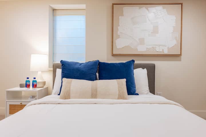 Drift into restful sleep in this quiet basement bedroom equipped with a queen bed and plush duvet bedding, soft and firm pillows, a sound machine, alarm clock, USB-C + A chargers, and Fiji water waiting to welcome you after a long day of travel.