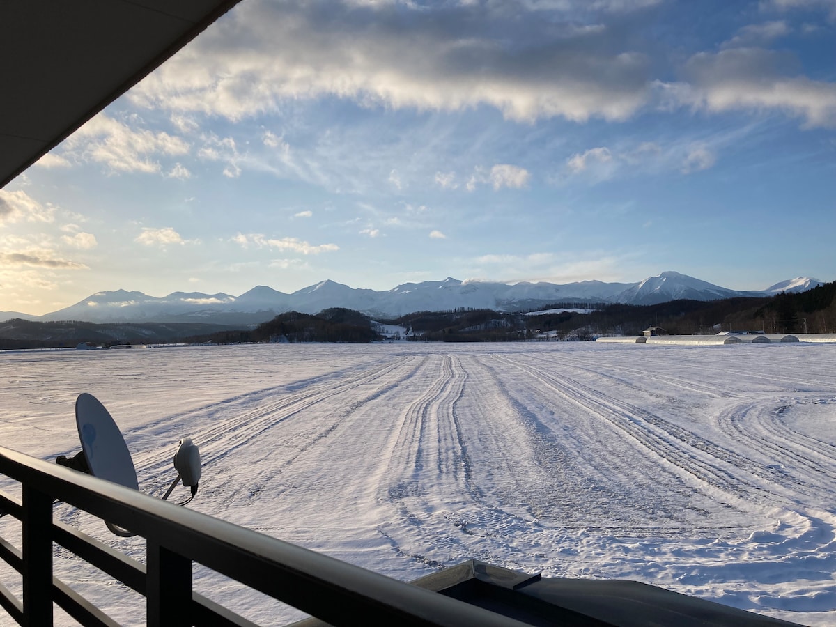 A winter landscape is displayed, featuring a vast expanse of snow-covered fields leading towards distant mountains under a partly cloudy sky. The scene includes satellite dishes in the foreground, emphasizing a peaceful, natural setting.