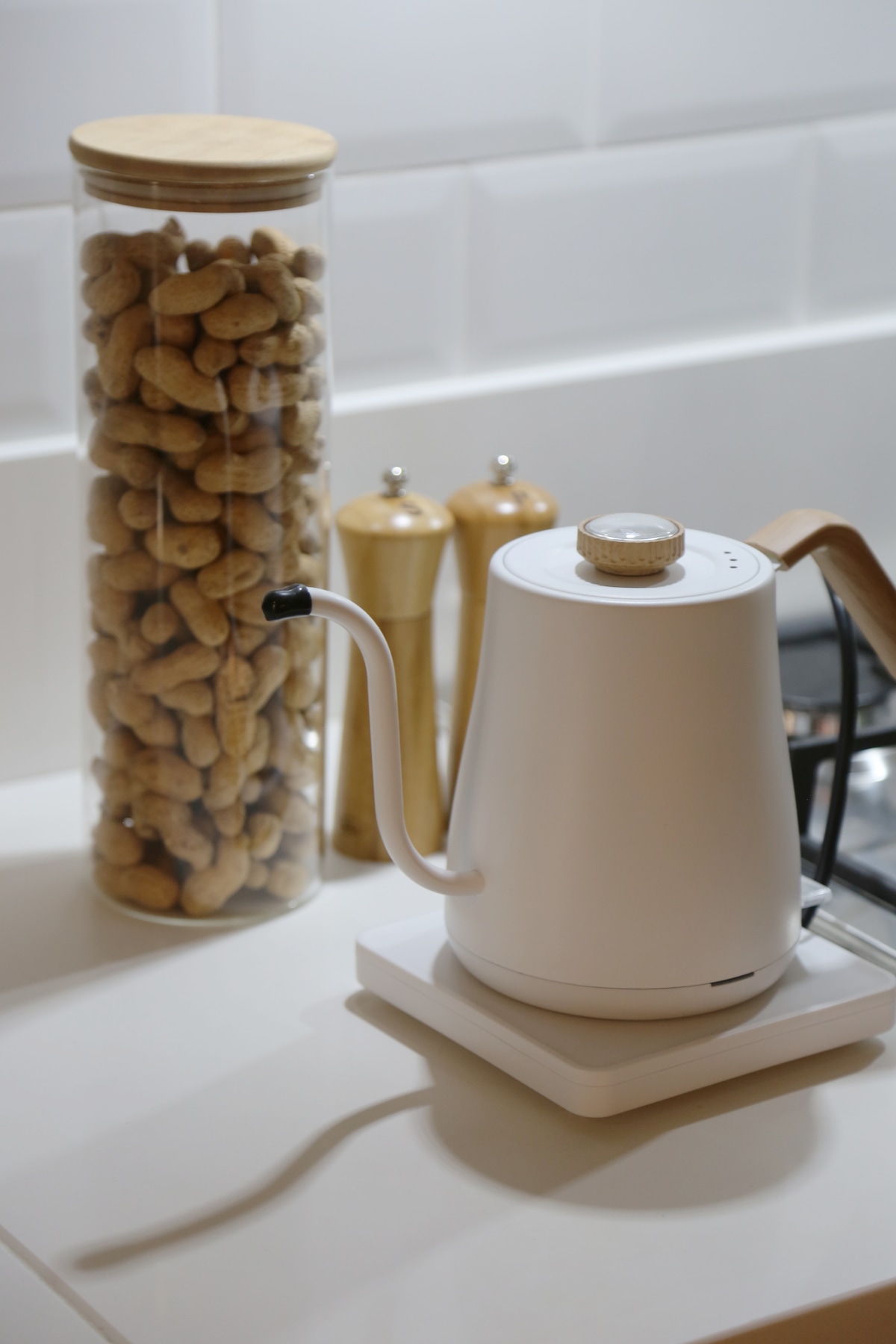 A modern electric kettle is positioned on a countertop, accompanied by a tall glass jar filled with nuts and two wooden pepper and salt shakers. The clean, minimalist design and neutral colors create a pleasant cooking space.