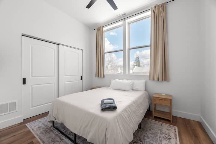 Një dhomë gjumi minimaliste me një prekje të rehatshme, që të çon në një hapësirë banimi të ndritshme dhe ftuese. Vepra artistike me tematikë malin shton një atmosferë të qetë dhe të frymëzuar nga natyra. ️✨