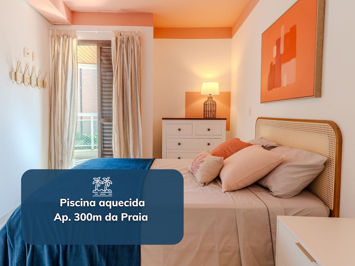 A well-lit bedroom showcases a spacious bed adorned with neutral-toned pillows and a decorative blanket. A nightstand with a lamp is positioned beside the bed, while light streams in through a window, complementing the soft color palette of the room.