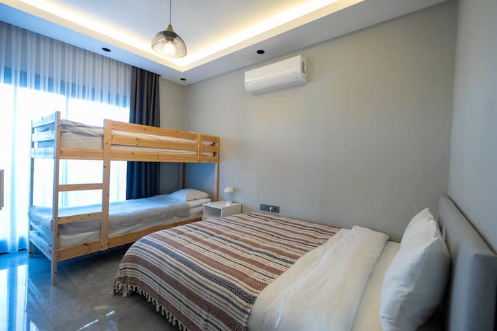 Dormitorio #2 (piso medio): vista al jardín y vista parcial al mar, cama tamaño queen, litera, armario con espejo, aire acondicionado/calentador, plancha y tabla de planchar. 