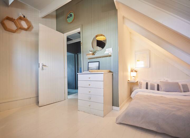 Dhomë gjumi e rehatshme me krevat dopio të vogël me raft dhe abazhur pranë krevatit dhe sirtarë për ruajtje.