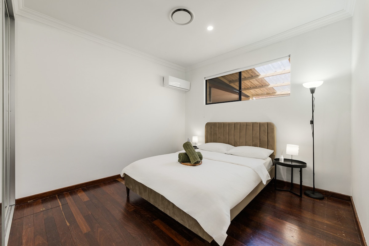 Თანამედროვე, მინიმალისტური ოთახი ორადგილიანი საწოლით, თეთრი თეთრეულით, კრემისფერი თავსაფრით და ორი მწვანე პირსახოცით. Ორი გვერდითი მაგიდა, თითოეულ მხარეს ლამპით. Ფანჯარა ჟალუზებით, კონდიციონერითა და ჭერის განათებით ავსებს სივრცეს.