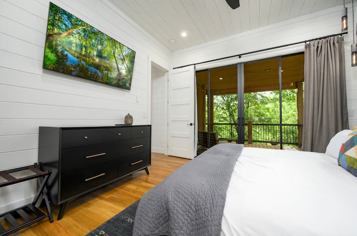 Wake up to peaceful nature views at “Hillside Hideaway” in a stylish bedroom with a cozy bed, modern decor, and a private balcony.
