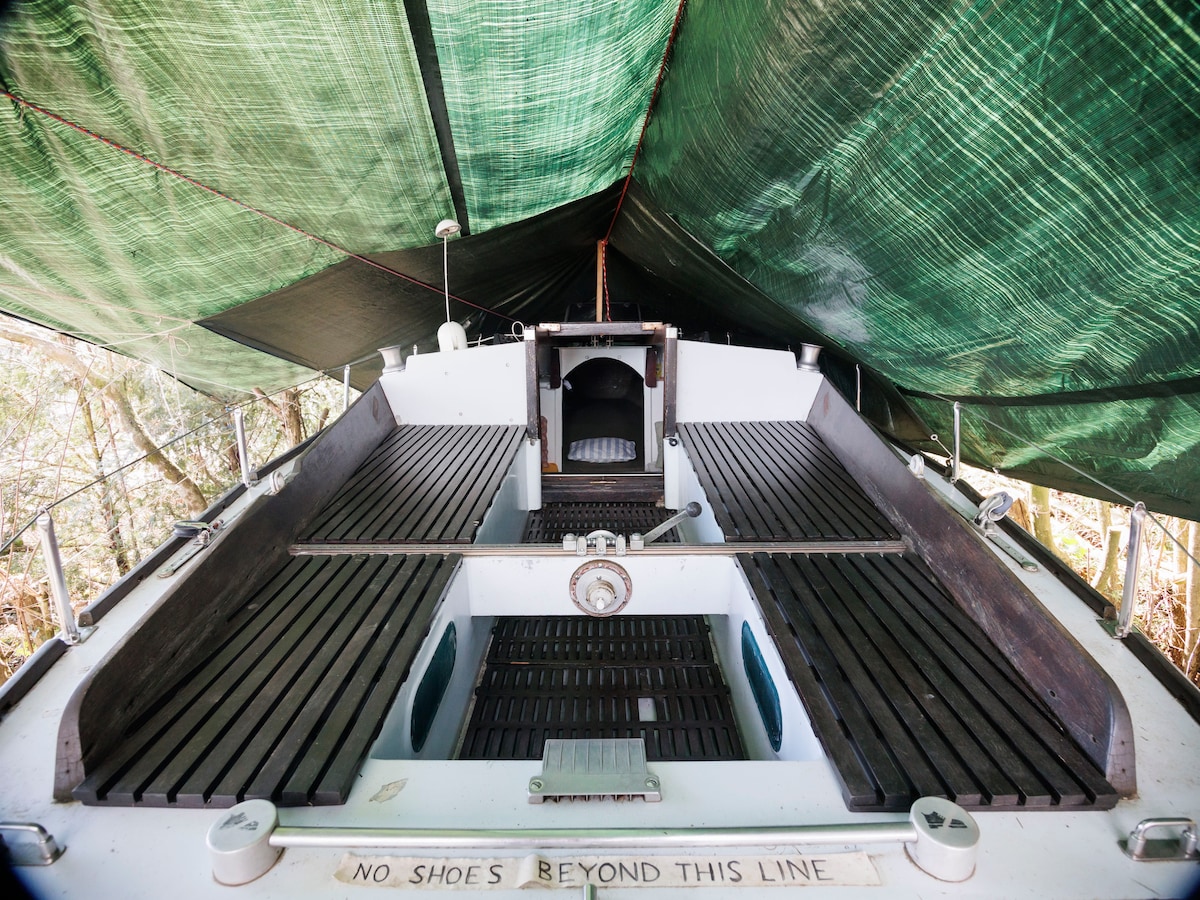 The interior of the boat is covered with a green tarp, creating a sheltered space. Wooden benches line the sides, creating areas for seating. A central entrance leads to an area with a steering wheel and controls. The floor is made of wooden slats.