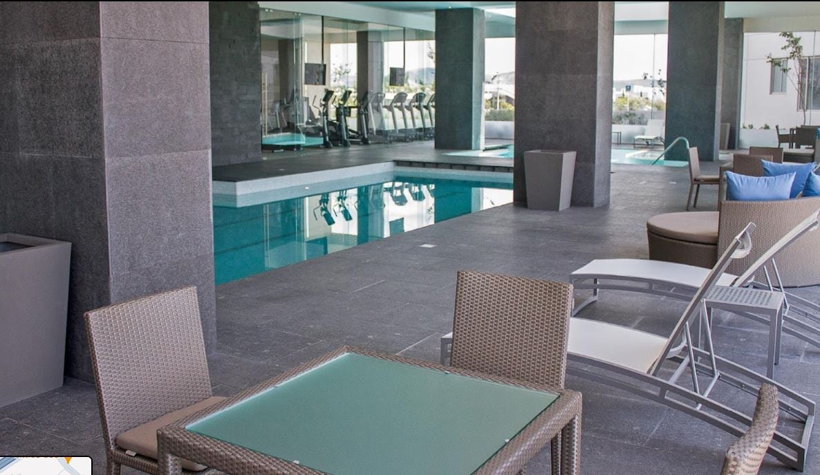 A modern pool area is featured, showcasing a clear swimming pool and spacious lounge chairs on a sleek tiled deck. A glassed-in fitness area is visible in the background, while a shaded seating arrangement offers a relaxing space for guests.