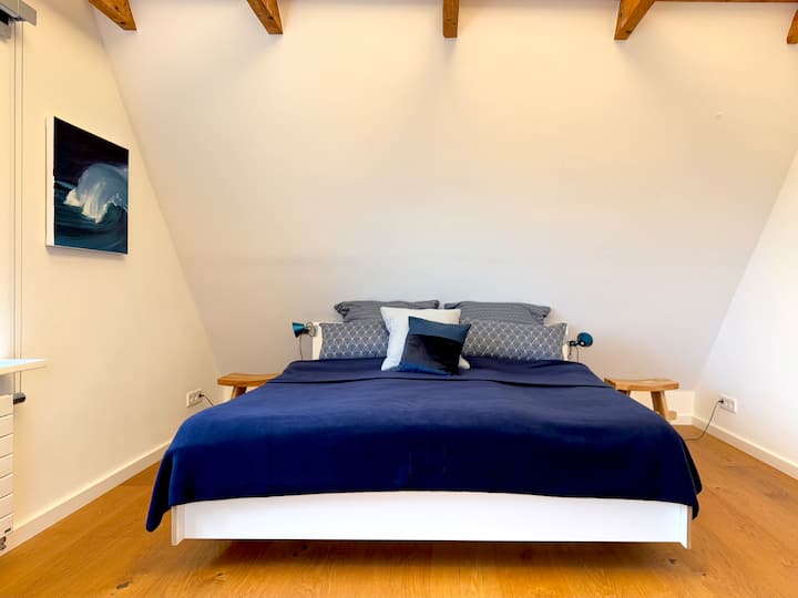 Nuestra cama en el primer dormitorio tiene 180 cm de ancho, puedes elegir entre diferentes almohadas. Las lámparas Artemide Tolomeo Micro de Italia proporcionan buena luz.