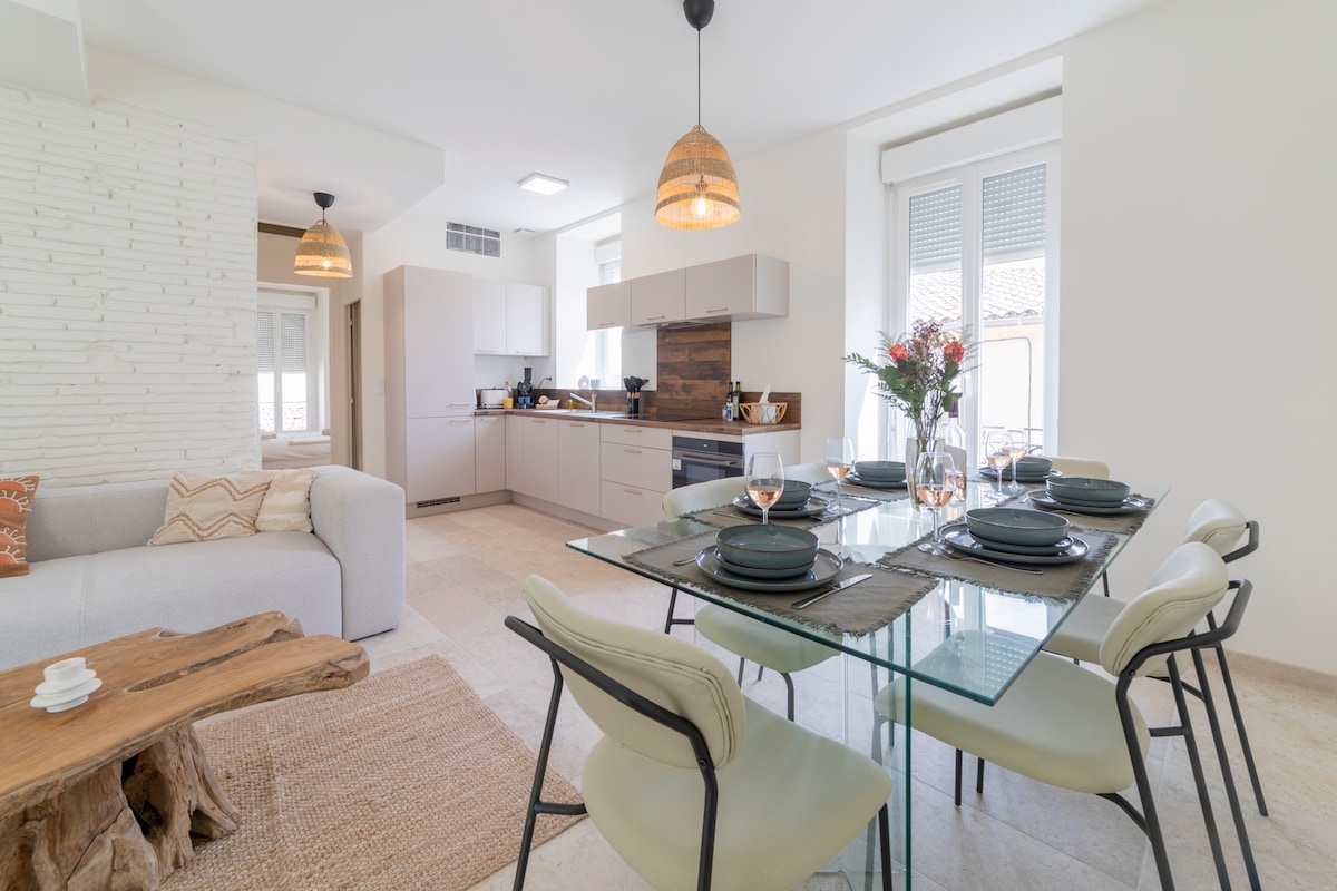 A modern dining area is set with a glass table and elegant chairs, accommodating six guests comfortably. Natural light illuminates the space, highlighting the neutral tones of the decor. A cozy sofa is positioned nearby, enhancing the inviting atmosphere of the open-plan living area.
